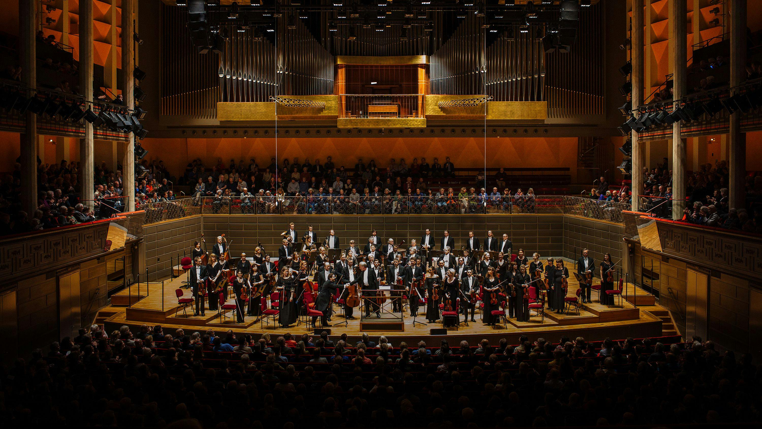 Interior view of the Konserthuset (Concert Hall) in Stockholm, Sweden, showcasing the Royal Stockholm Philharmonic Orchestra on stage receiving applause from a full audience.